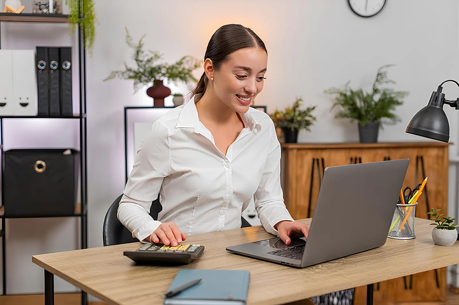 An accounting assistant working on a laptop with a calculator